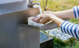 World water day concept. Woman washing hands with tap water under faucet at stainless steel sink. Washing hands with tap water at outdoor sink. Personal hygiene. Water consumption and sustainability. photo