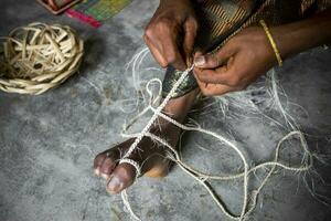 An woman is making a rope from the fibers of a banana tree with the help of her feet in an ancient way at at Madhupur, Tangail, Bangladesh. photo