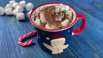 Hot chocolate in mug with ginger breadman on blue wooden table. Candy and marshmallows. video
