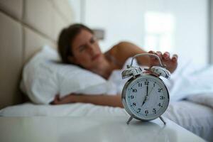 Woman lying in bed turning off an alarm clock in the morning at 5am. Hand turns off the alarm clock waking up at morning, girl turns off the alarm clock waking up in the morning from a call. photo