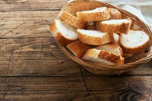 Fresh white bread, baguette slices in a wicker basket. Wooden rustic table background. Copy space photo