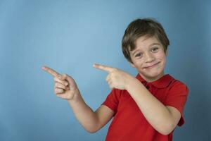 A cute Caucasian boy in a red T-shirt is assertively and cheerfully pointing his hands and fingers to the side photo
