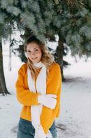 adolescente rubia en un amarillo suéter fuera de en invierno. un Adolescente niña en un caminar en invierno ropa en un Nevado bosque foto