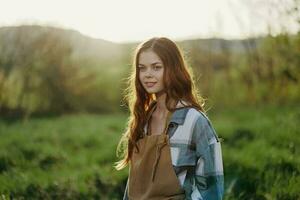 Portrait of a young smiling woman in work clothes checkered shirt and apron in nature in the evening after work photo