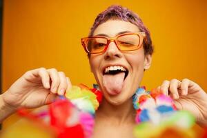 Portrait of a woman with a floral Hawaiian wreath around her neck is having fun dancing and smiling in bright clothes on an orange background wearing sunglasses, lifestyle party Hawaiian style photo