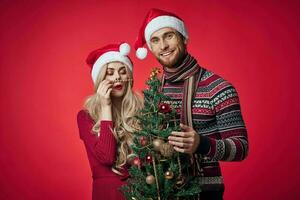 cute young couple holding christmas tree toys decoration red background photo