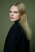 A beautiful girl looks half-turned into the camera at you posing on a green background in a jacket in the studio photo