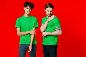 Two cheerful friends in green t-shirts communicating emotions red background photo