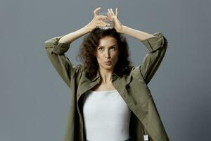 Funny pretty curly beautiful woman in casual khaki green shirt hold glass of water overhead posing isolated on over gray blue background. Healthy lifestyle. Water is Life concept. Copy space photo