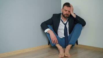 Desperate bearded man in untidy formal clothes is sitting in an empty apartment. The effects of the Covid-19 virus on the economy are unemployment, poverty, and disease. video