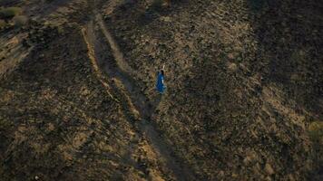 Top view of woman in a beautiful blue dress walking throuht the nature reserve. Sparse vegetation, rocky soil, arid climate. Tenerife, Canary Islands, Spain video
