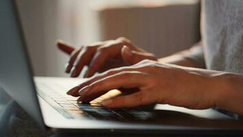 Female hands typing on a laptop keyboard against the setting sun. Concept of remote work. Home Office video