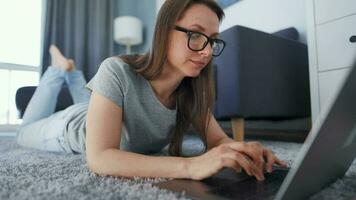 donna è dire bugie su il pavimento e Lavorando su un' il computer portatile. concetto di a distanza opera. video