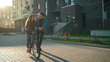 Dad is teaching daughter how to ride bicycle at sunset video