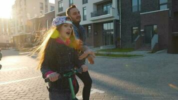 Dad is teaching daughter how to ride a scooter at sunset video