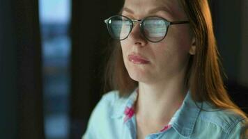 mujer en lentes mirando en el monitor y surf Internet a noche. el monitor pantalla es reflejado en el lentes. extremadamente cerca arriba. trabajo a noche. hogar oficina. remoto trabajo video