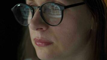 Woman in glasses looking on the monitor and surfing Internet at night. The monitor screen is reflected in the glasses. Extremely close up. Work at night. Home Office. Remote work video