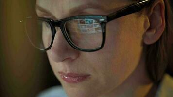 Woman in glasses looking on the monitor and surfing Internet at night. The monitor screen is reflected in the glasses. Extremely close up. Work at night. Home Office. Remote work video