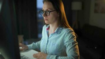 Frau im Brille suchen auf das Monitor und Surfen Internet beim Nacht. das Monitor Bildschirm ist reflektiert im das Brille. äußerst schließen hoch. Arbeit beim Nacht. Zuhause Büro. Fernbedienung Arbeit video