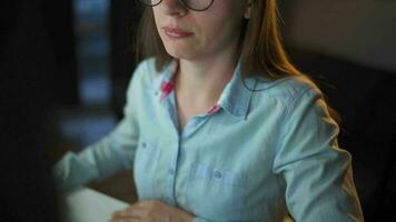 mujer en lentes mirando en el monitor y surf Internet a noche. el monitor pantalla es reflejado en el lentes. extremadamente cerca arriba. trabajo a noche. hogar oficina. remoto trabajo video