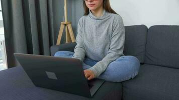 mulher sentado em uma acolhedor sofá e trabalhando em uma computador portátil. conceito do controlo remoto trabalhar. casa escritório video