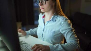 Frau im Brille suchen auf das Monitor und Surfen Internet beim Nacht. das Monitor Bildschirm ist reflektiert im das Brille. äußerst schließen hoch. Arbeit beim Nacht. Zuhause Büro. Fernbedienung Arbeit video