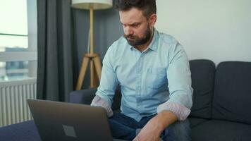 Man sitting on a cozy sofa and working on laptop and smartphone. Concept of remote work. Home Office video