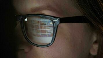 Woman in glasses looking on the monitor and surfing Internet at night. The monitor screen is reflected in the glasses. Extremely close up. Work at night. Home Office. Remote work video