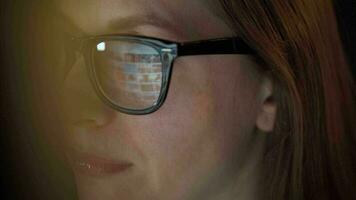 Woman in glasses looking on the monitor and surfing Internet at night. The monitor screen is reflected in the glasses. Extremely close up. Work at night. Home Office. Remote work video