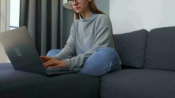 vrouw zittend Aan een knus sofa en werken Aan een laptop. concept van afgelegen werk. huis kantoor video