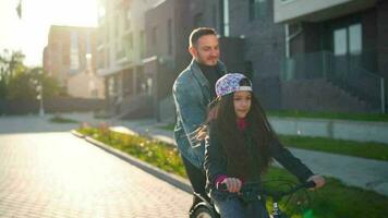 Dad is teaching daughter how to ride bicycle at sunset video