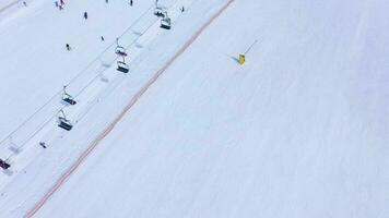 Ski slope - ski lift, skiers and snowboarders going down. Aerial view video