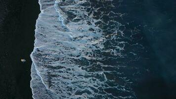 Top view of a girl in a blue dress and hat walking on the beach with black sand, foaming waves of the Atlantic Ocean. Tenerife, Canary Islands, Spain video