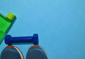 blue dumbbell and sneakers indicating workout plan on blue background. Top view with copy space for any design. Healthy and fitness concept photo