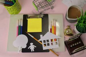 Top view of the cutting paper or drawing house on a pink table, preparing to do homework in a clipboard. Drawing Working Desk Concept photo