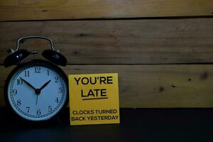 You're Late - Clocks Turned Back Yesterday write on a sticky note isolated on wooden background. photo