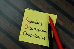 SOC - Standard Occupational Classification write on sticky notes isolated on Wooden Table. photo