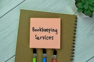 Concept of Bookkeeping Services write on sticky notes isolated on Wooden Table. photo