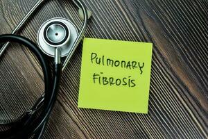 Concept of Pulmonary Fibrosis write on sticky notes with stethoscope isolated on Wooden Table. photo