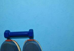 blue dumbbell and sneakers indicating workout plan on blue background. Top view with copy space for any design. Healthy and fitness concept photo