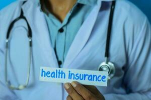 Doctor holding a card with text health insurance. Medical and healthcare concept. photo