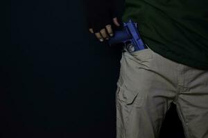 asian man holds a gun. Gun in his pants isolated on black background. photo