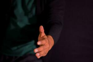 Young man giving hand for shaking on dark black background. selective focus on finger photo