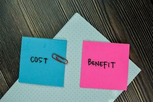 Cost and Benefit write on sticky note and isolated on Wooden Table. Finance Concept photo