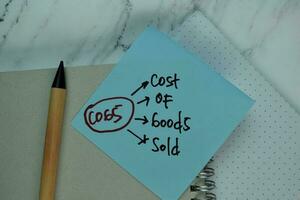 COGS - Cost Of Goods Sold write on sticky note isolated on Wooden Table. photo