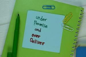 Under Promise and Over Deliver write on sticky note isolated on Wooden Table. photo