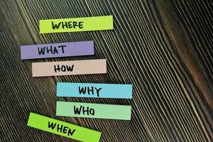 Where, What, How, Why, Who, When write on sticky note and isolated on Wooden Table. photo