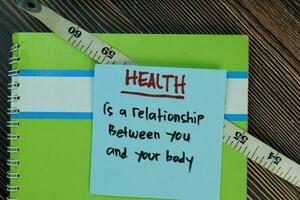 Health is a relationship between you and your body write on sticky notes isolated on Wooden Table. Motivation concept photo