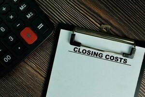 Closing Costs write on a paperwork isolated on Wooden Table. photo