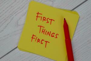 First Things First write on sticky notes isolated on Wooden Table. photo